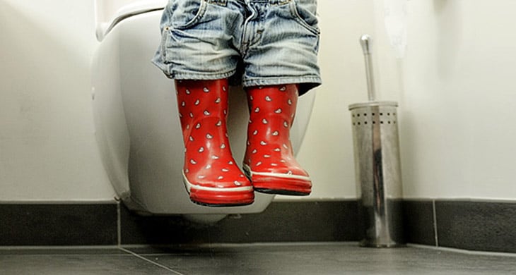 Foto van klein kindje dat op de wc zit met rode laarsjes aan