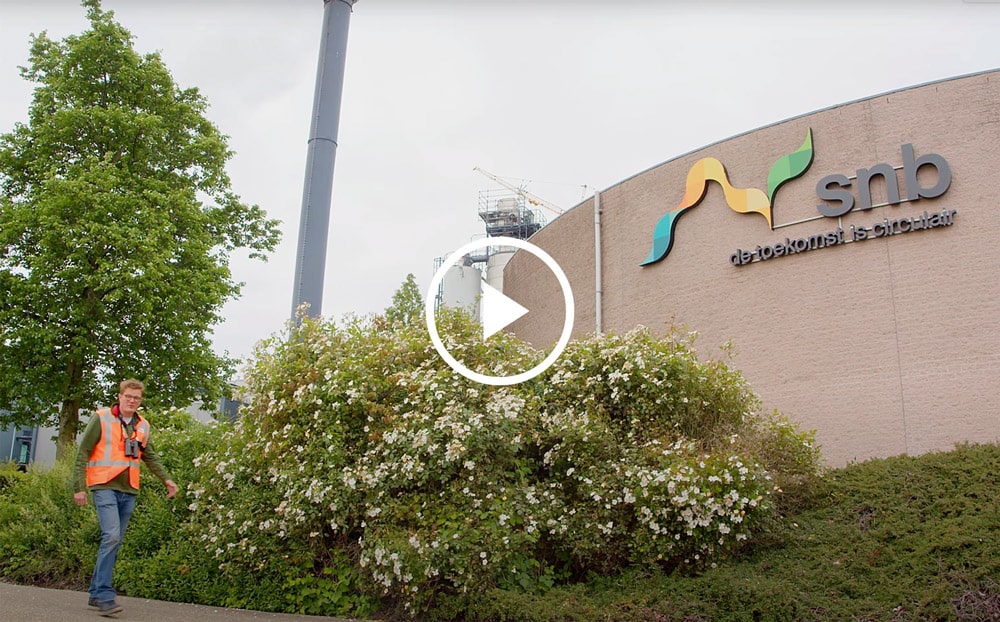Man die voor het gebouw van SNB loopt en de natuur rondom het gebouw laat zien.